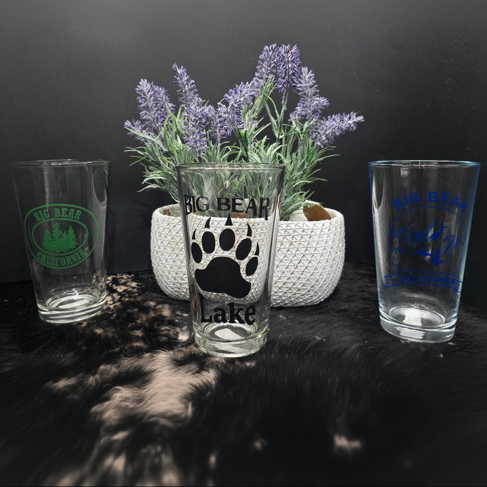 assorted Big Bear California themed pint beer glasses featuring bear paw mountain and forest logo designs for rustic cabin and lodge drinkware