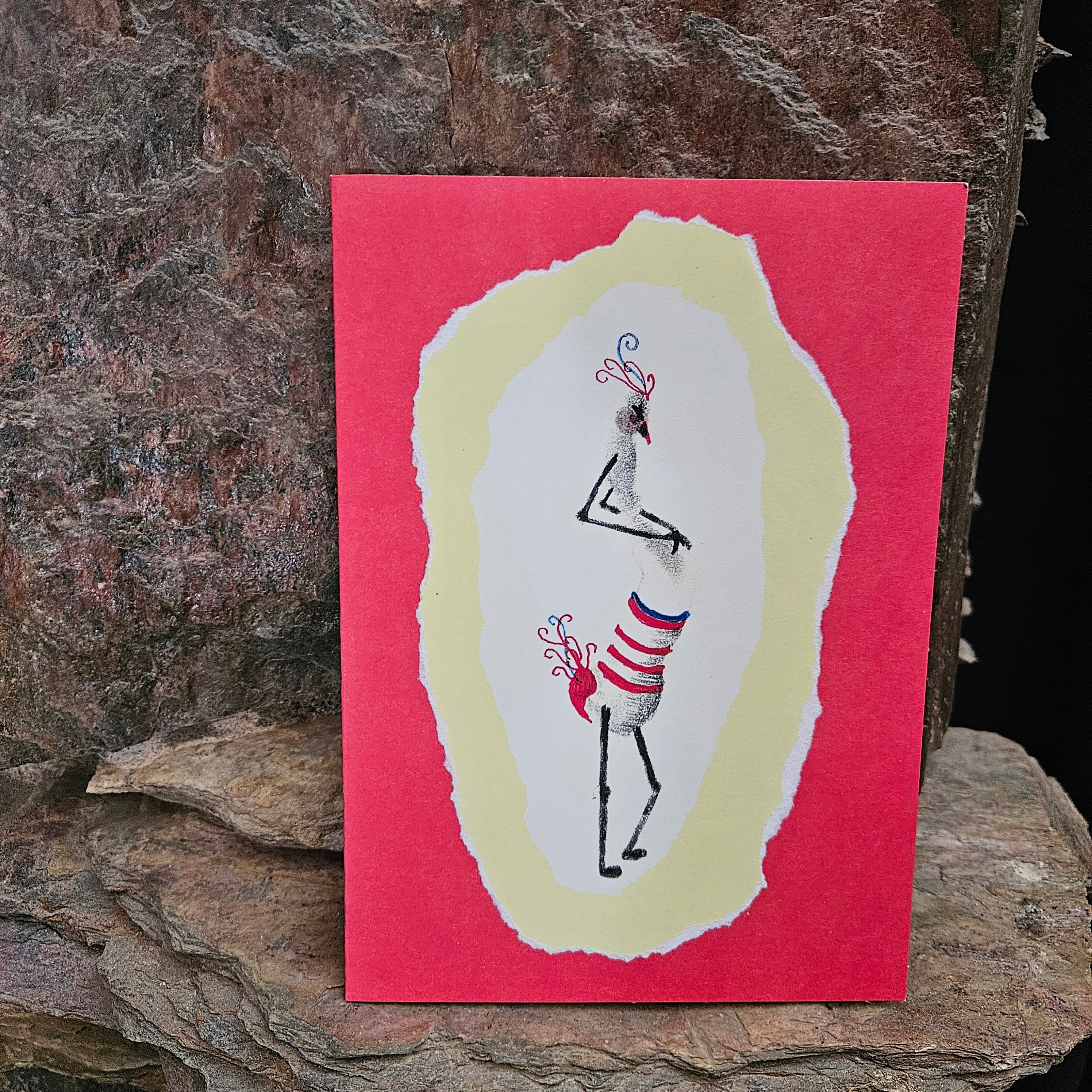 A handcrafted greeting card with a colorful abstract fingerprint design figure on a red background, displayed against a natural stone backdrop.