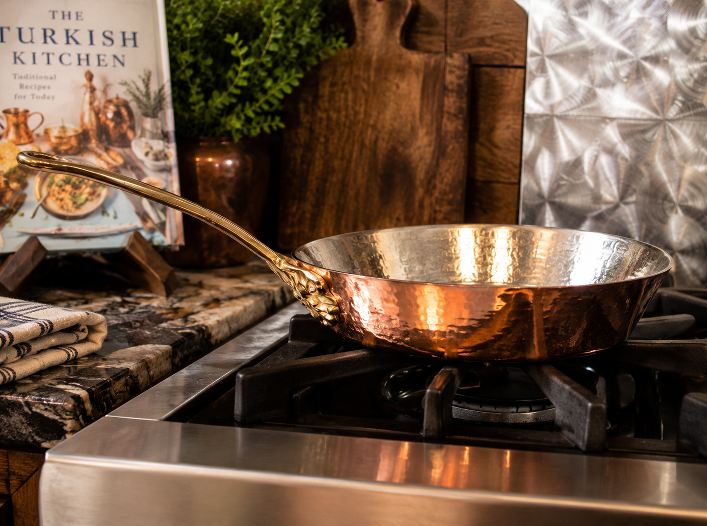 Hak Art solid copper frying pan handcrafted in Turkey featuring a hammered copper finish and decorative brass-tone handle displayed on a stovetop.