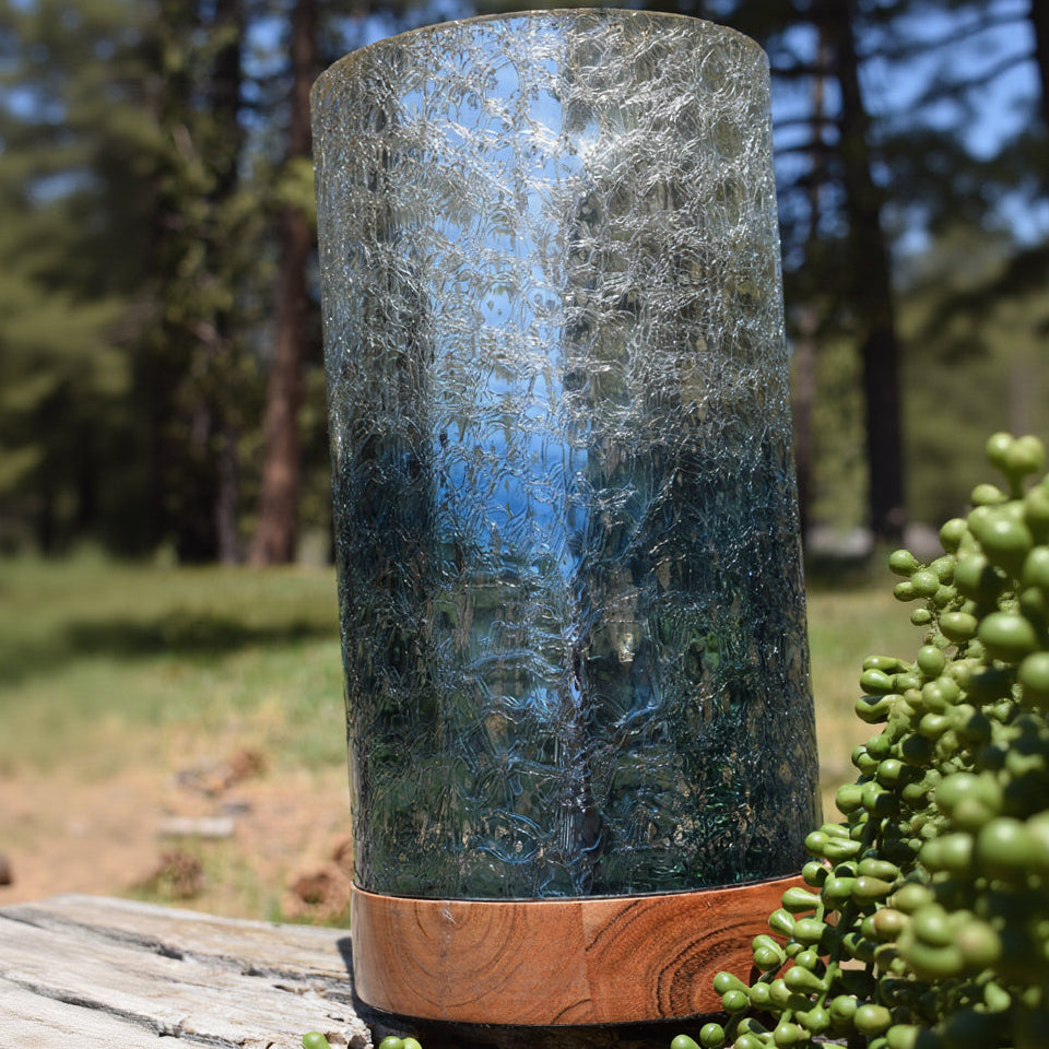 Cylindrical glass lantern with wooden base in a forest setting