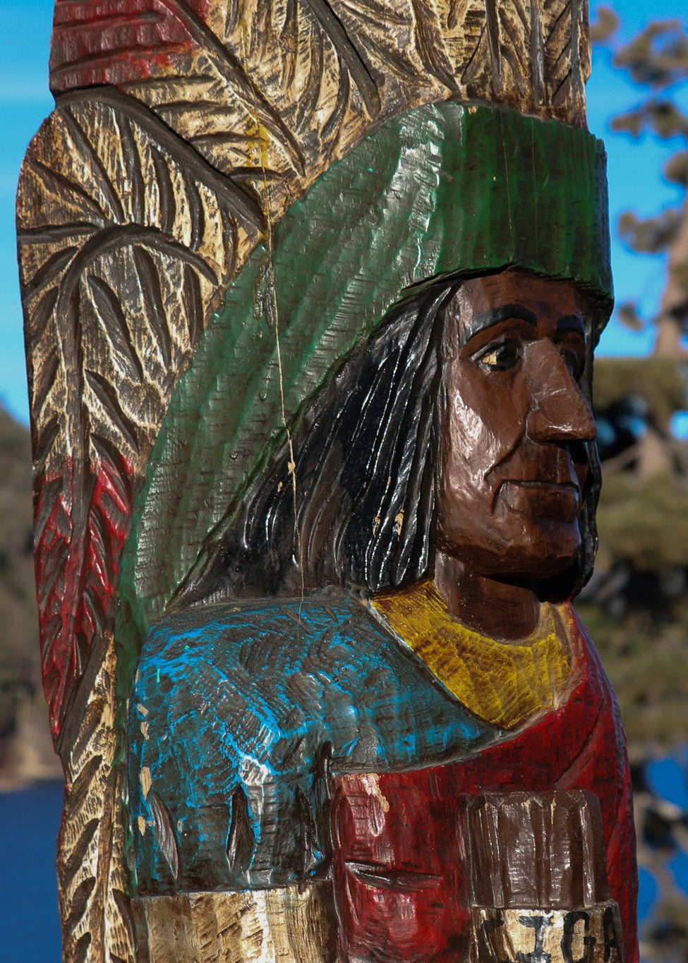 Wooden carving of a Native American figure with colorful clothing against a natural background