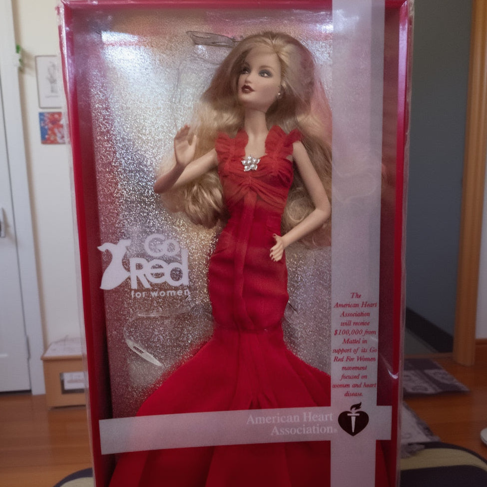 Barbie doll in a red dress with 'Go Red for Women' packaging, featuring the American Heart Association logo.