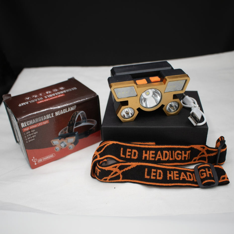 A USB rechargeable headlamp with built-in battery, displayed alongside its packaging. The headlamp is black with silver/gold accents, and there is an LED headlight strap