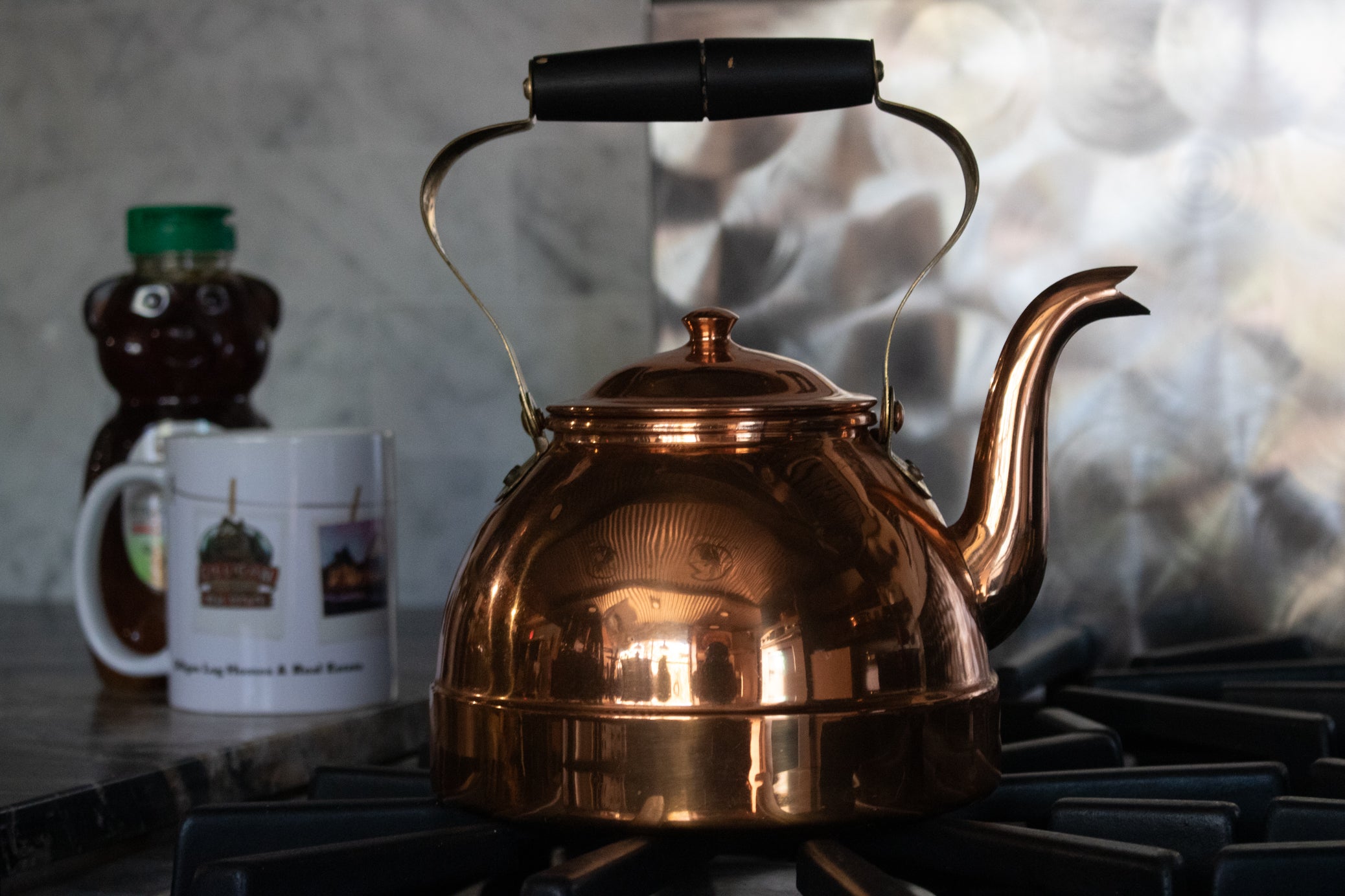 vintage NASCO copper tea kettle made in Colombia with polished copper finish curved spout and overhead handle displayed on stovetop