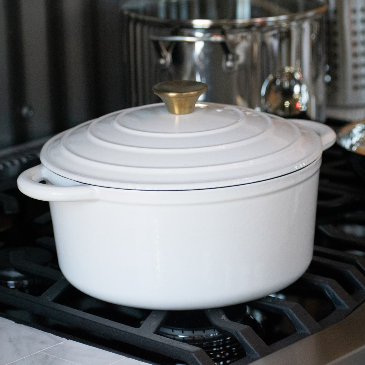 A white enameled cast iron Dutch oven with a gold stainless steel knob on the lid Biltmore Enameled 5.2 Qt. Cast Iron Dutch Oven with Matching Lid
