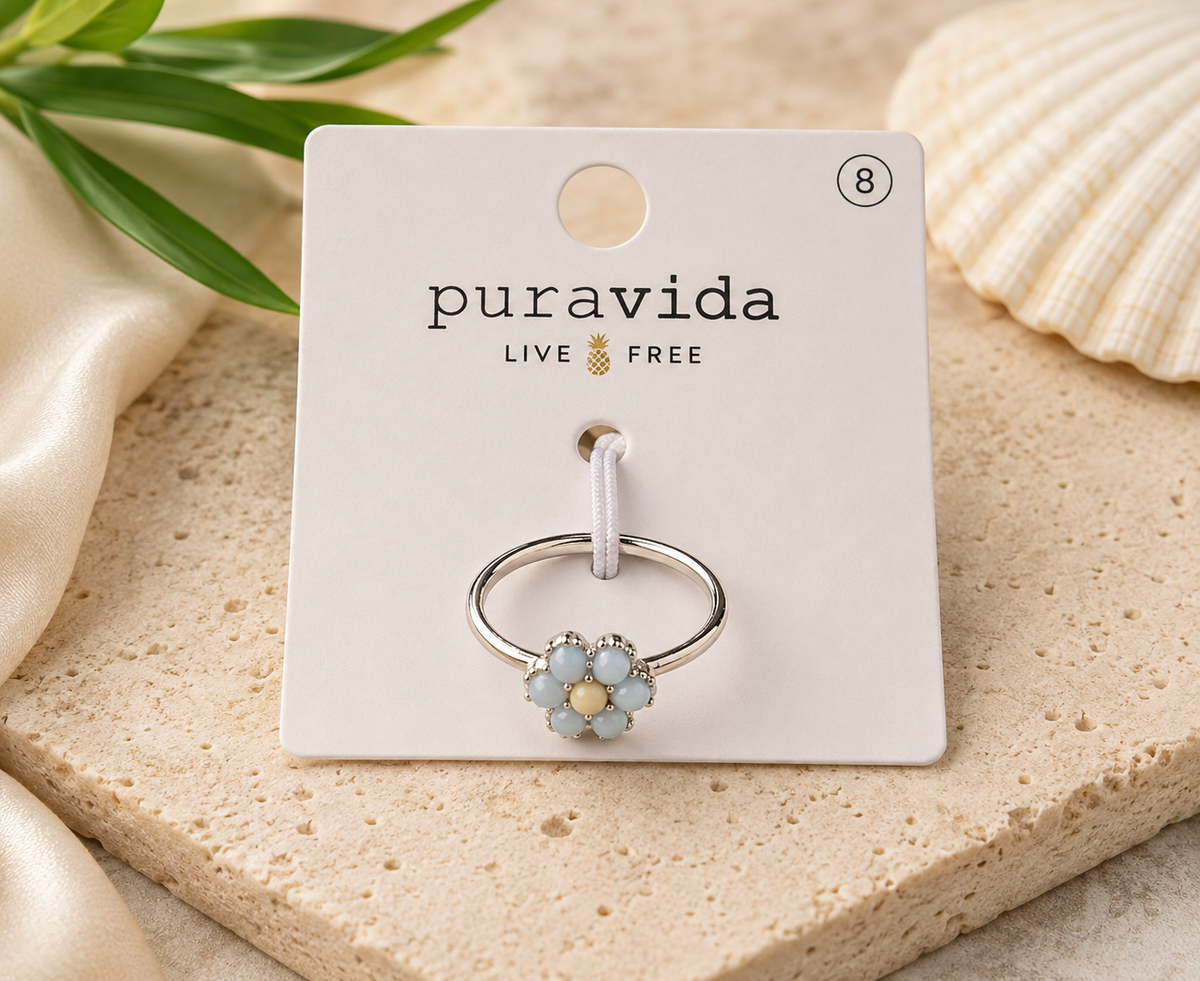 Authentic Pura Vida silver-tone ring featuring a light blue daisy flower with a cream center on a slim band, displayed on its original Pura Vida card