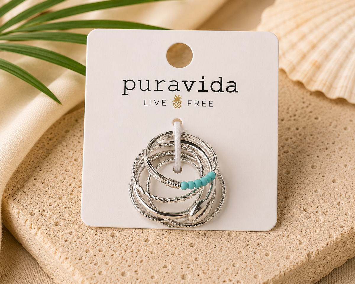 Authentic Pura Vida silver-tone stackable ring set featuring multiple textured bands with turquoise-colored bead accents and a polished shell charm, displayed new on the original branded card.