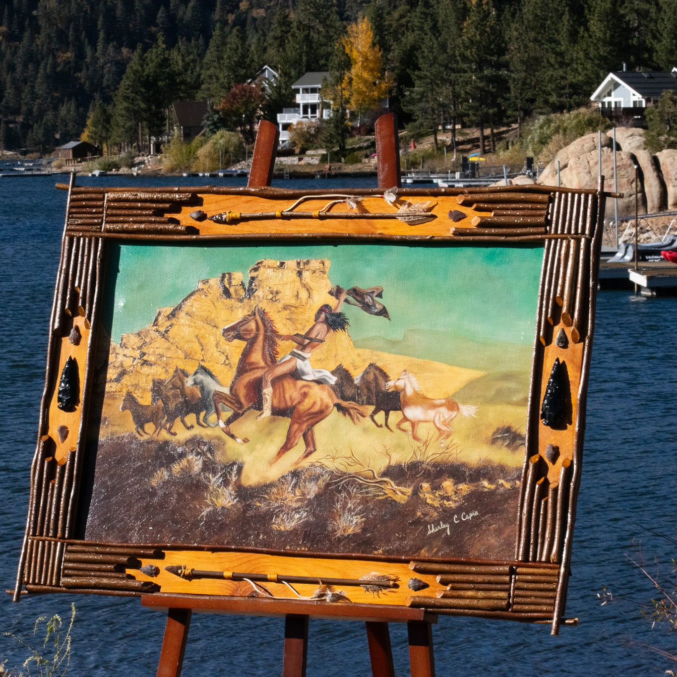 large framed western artwork titled War Indian on Bareback by Shirley C Capra featuring Native American rider on horseback in handcrafted rustic frame with arrowheads antlers and natural wood accents