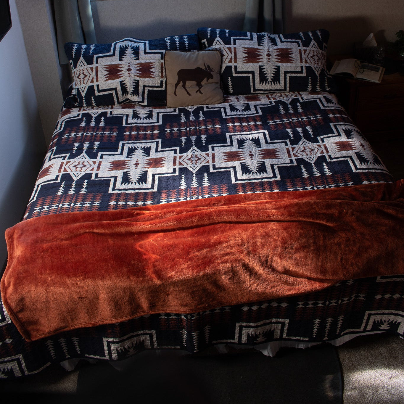 A queen-sized bed with a Pendleton Harding Southwestern Geometric Oxford Wool Blanket in navy blue, white, and burnt orange, along with coordinating pillowcases.