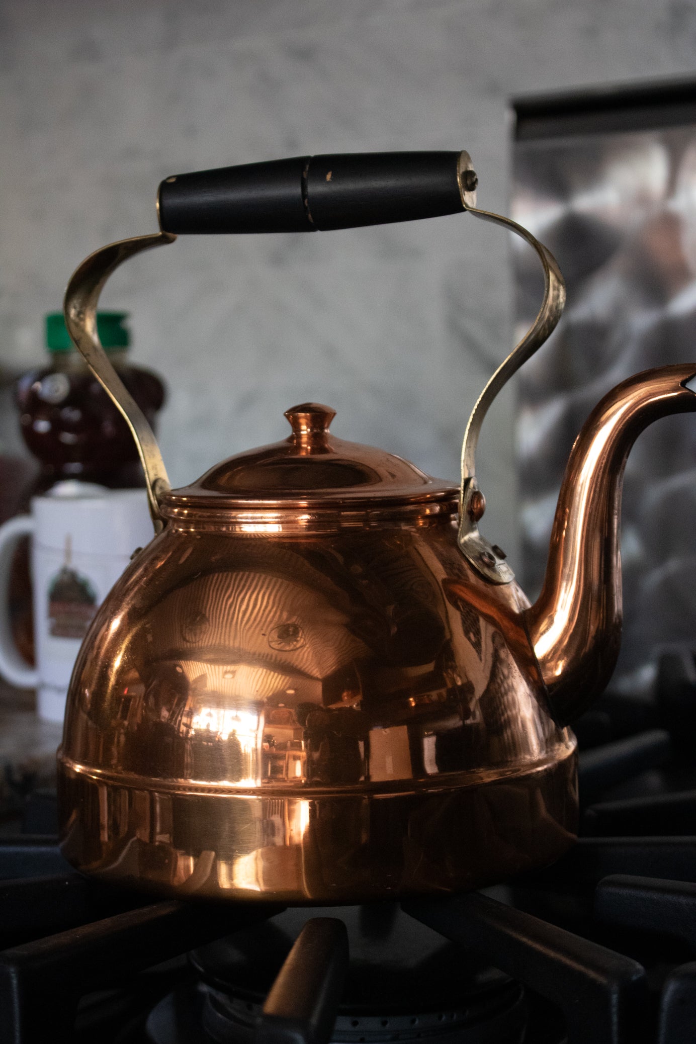 vintage NASCO copper tea kettle made in Colombia with polished copper finish curved spout and overhead handle displayed on stovetop