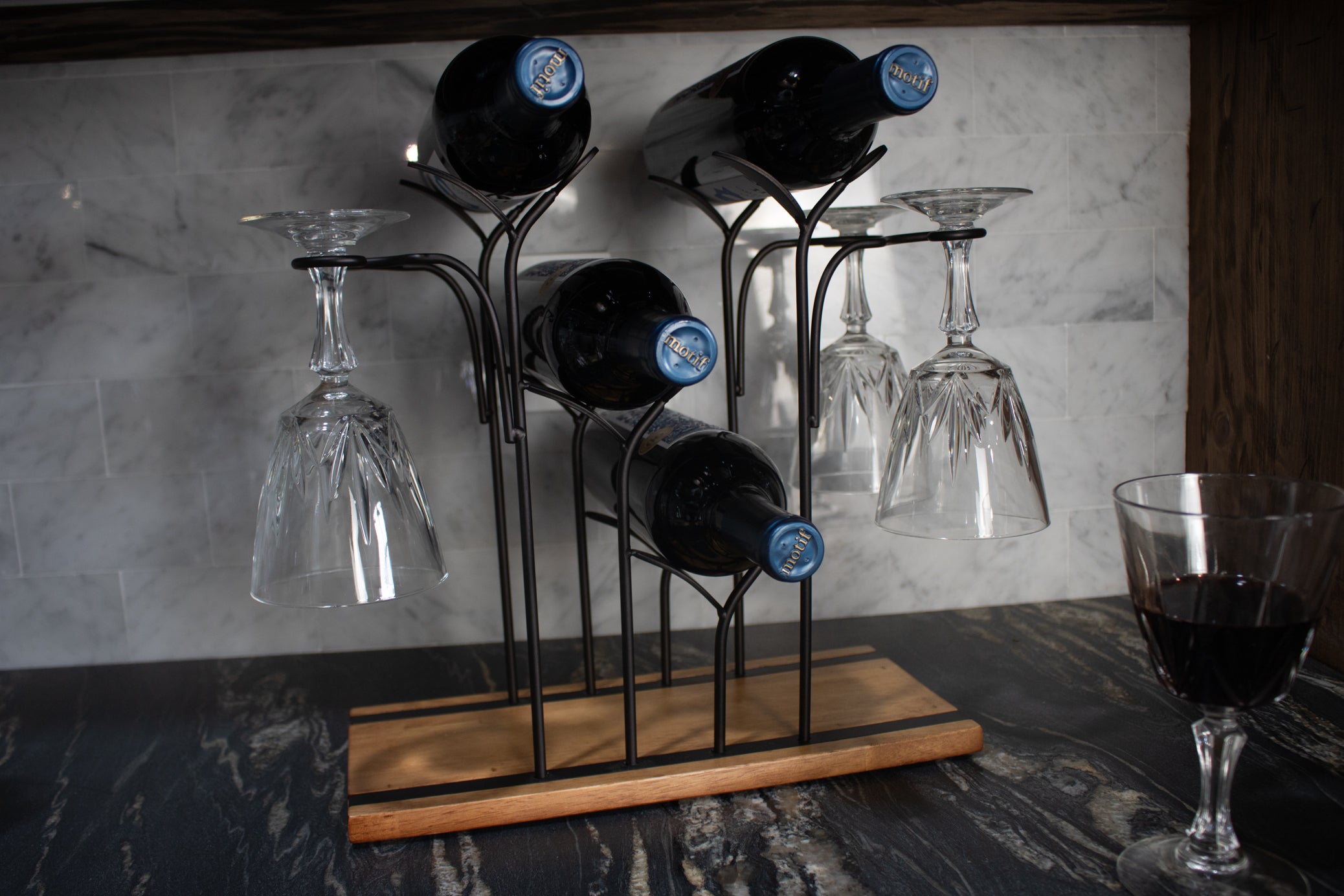 black metal wine bottle and stemware display rack with rustic wood base holding wine bottles and hanging wine glasses