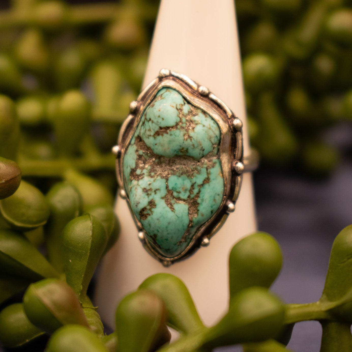A faux turquoise gemstone ring with a metal band and detailed border